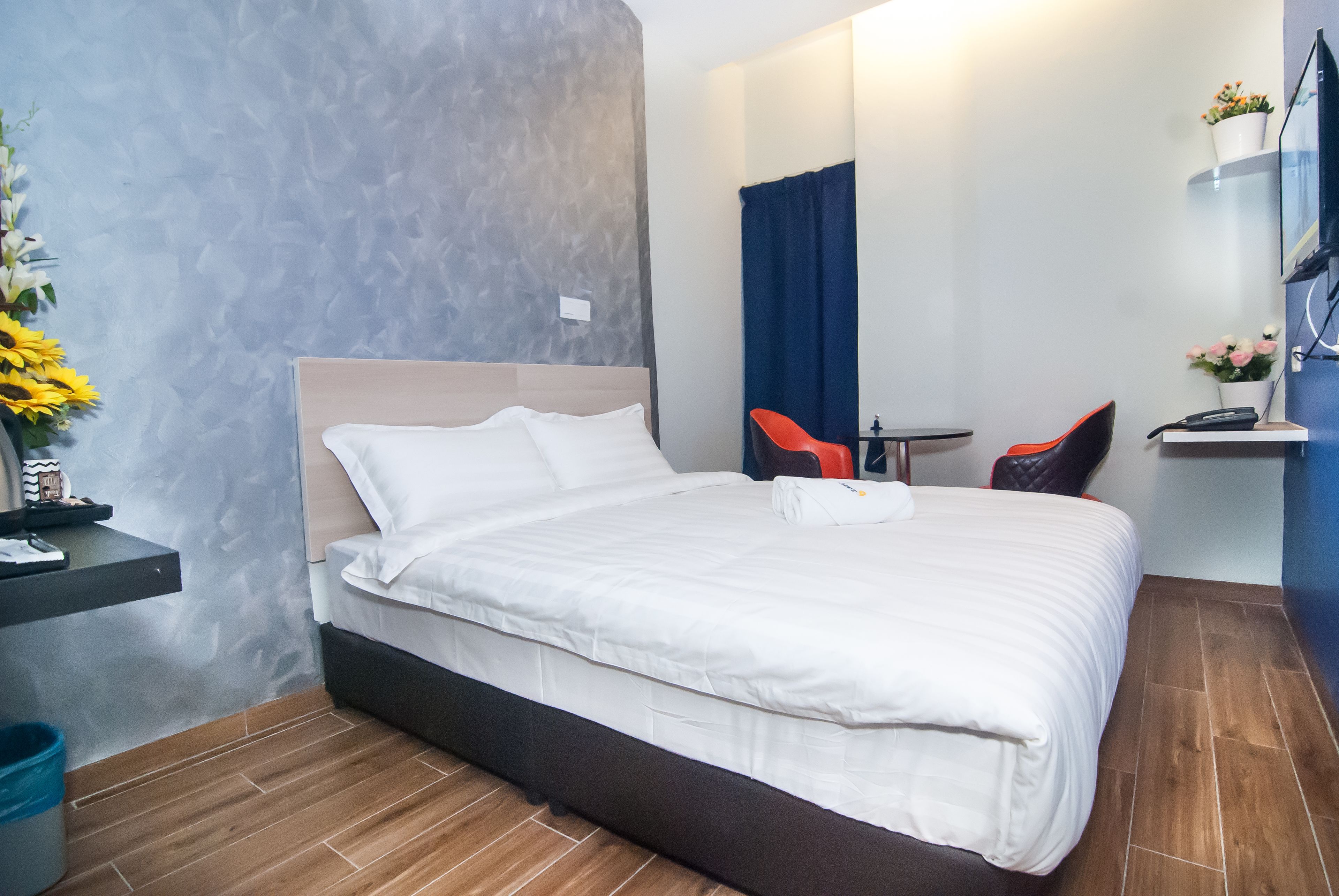 A neatly made bed with white linens, a small bedside table with a lamp, a chair, and a desk with a chair.