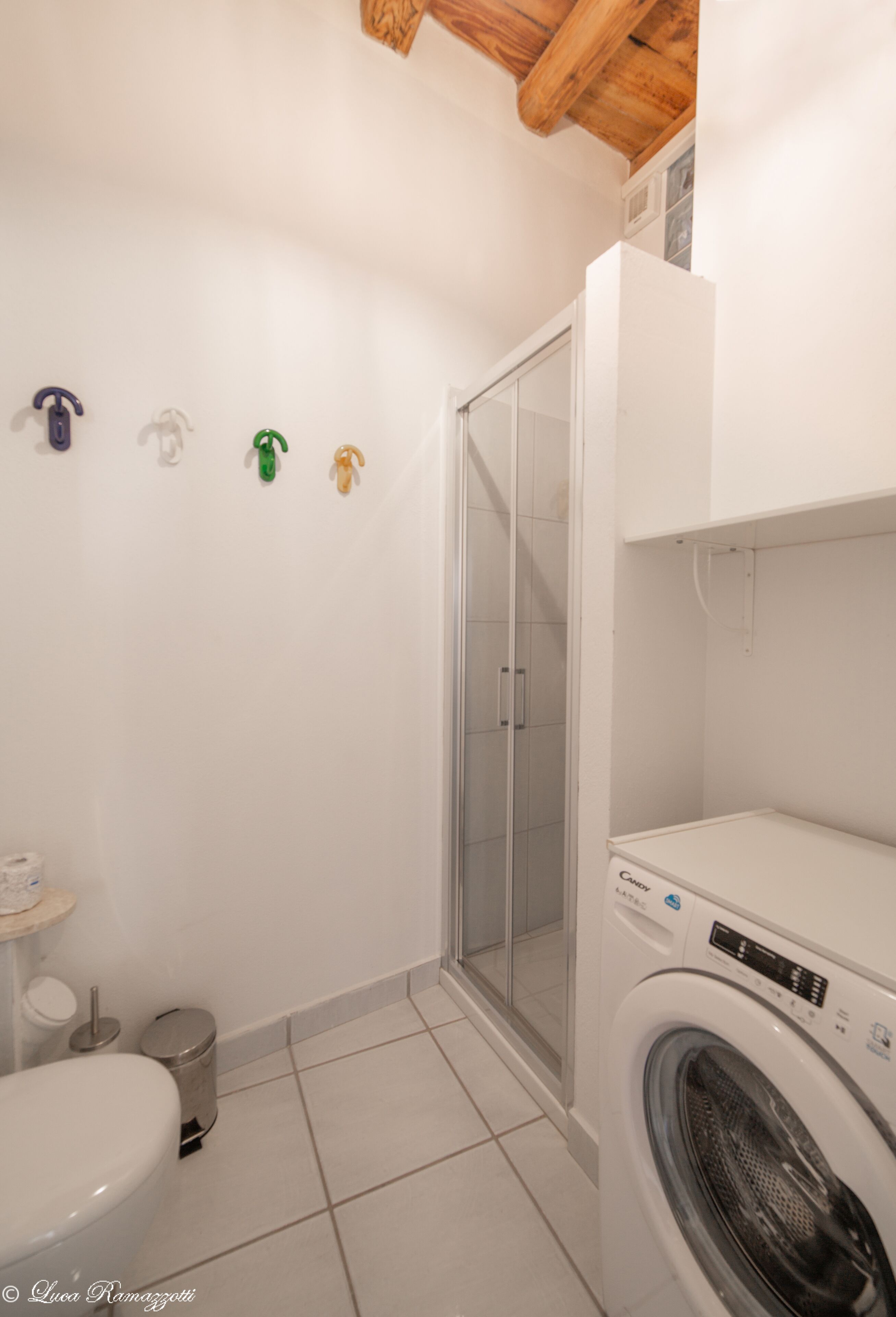 Et badeværelse med toilet, vaskemaskine og brusekabine i glas.