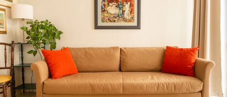 Un canapé beige agrémenté de coussins orange, un tableau abstrait encadré, une plante verte et un tapis à motifs.