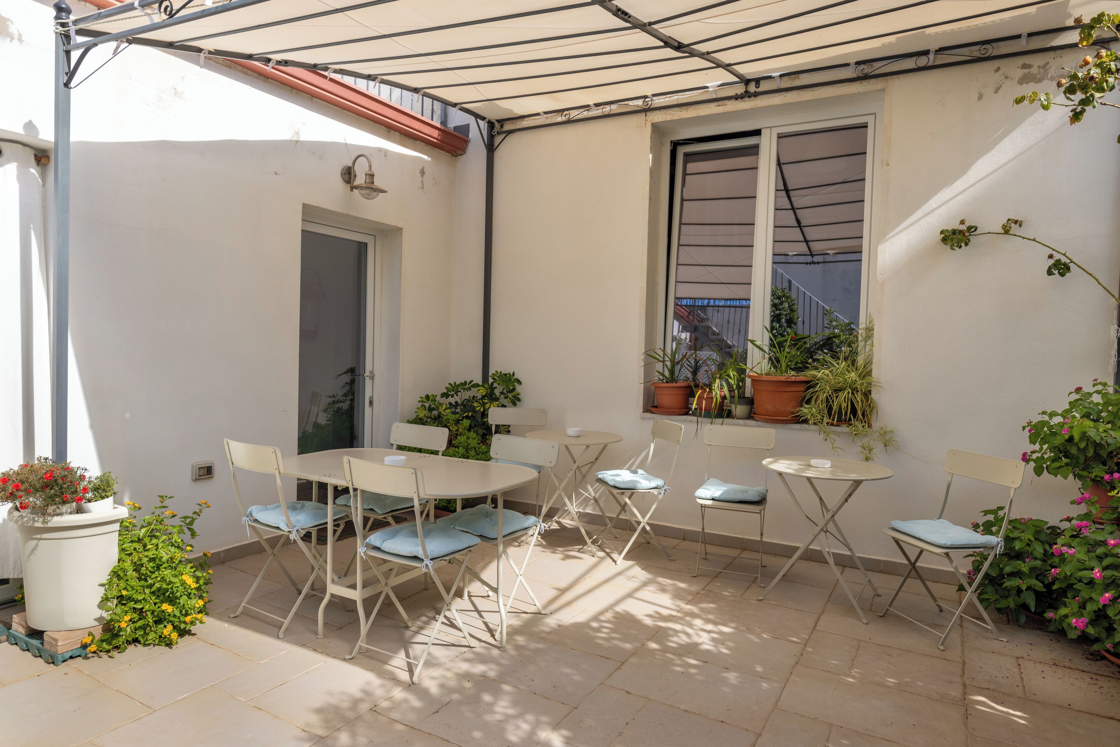 A patio with a table and chairs, potted plants, and a window.