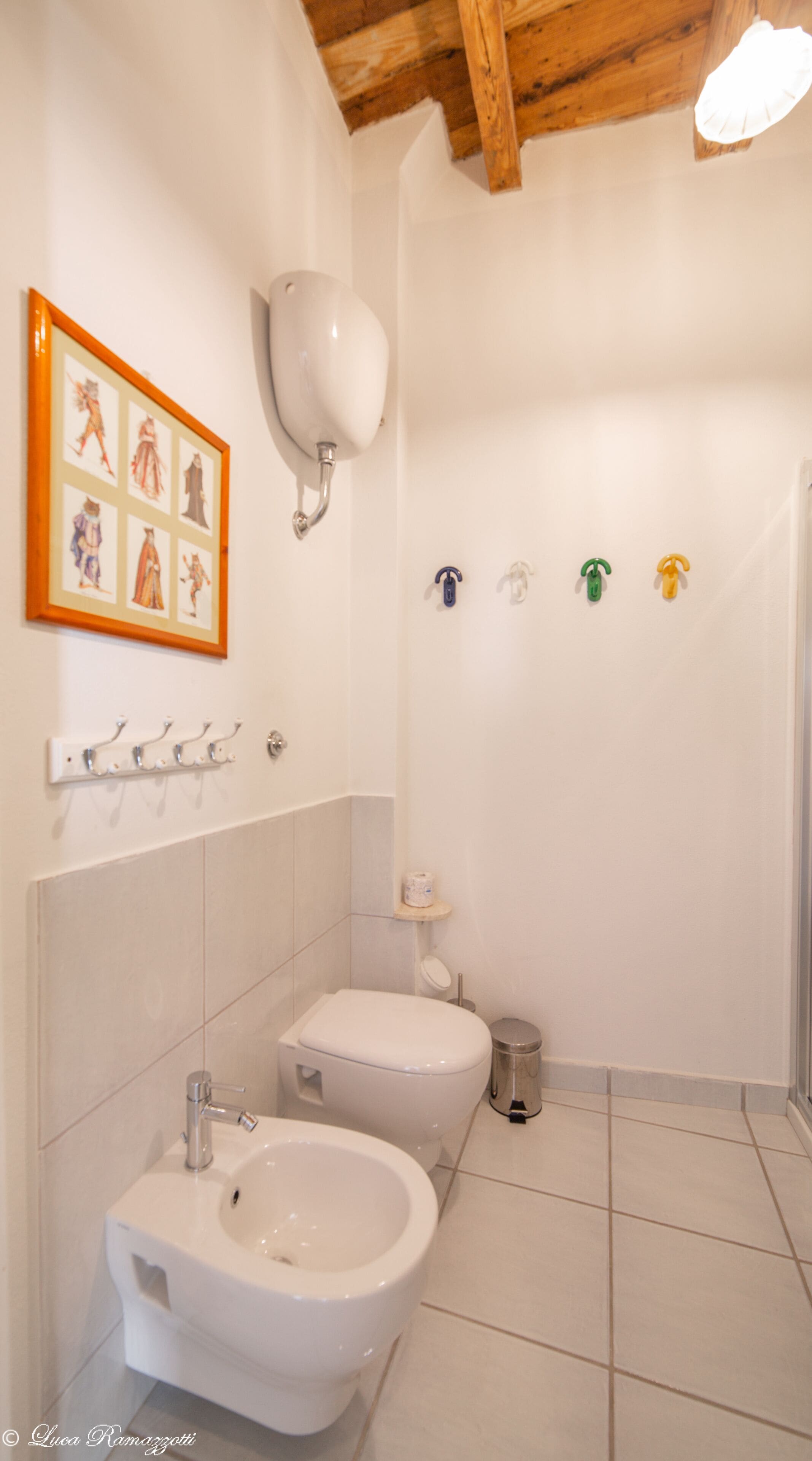 A bathroom with a bidet, toilet, and a sink. There is a framed picture on the wall and a small shelf with toiletries.