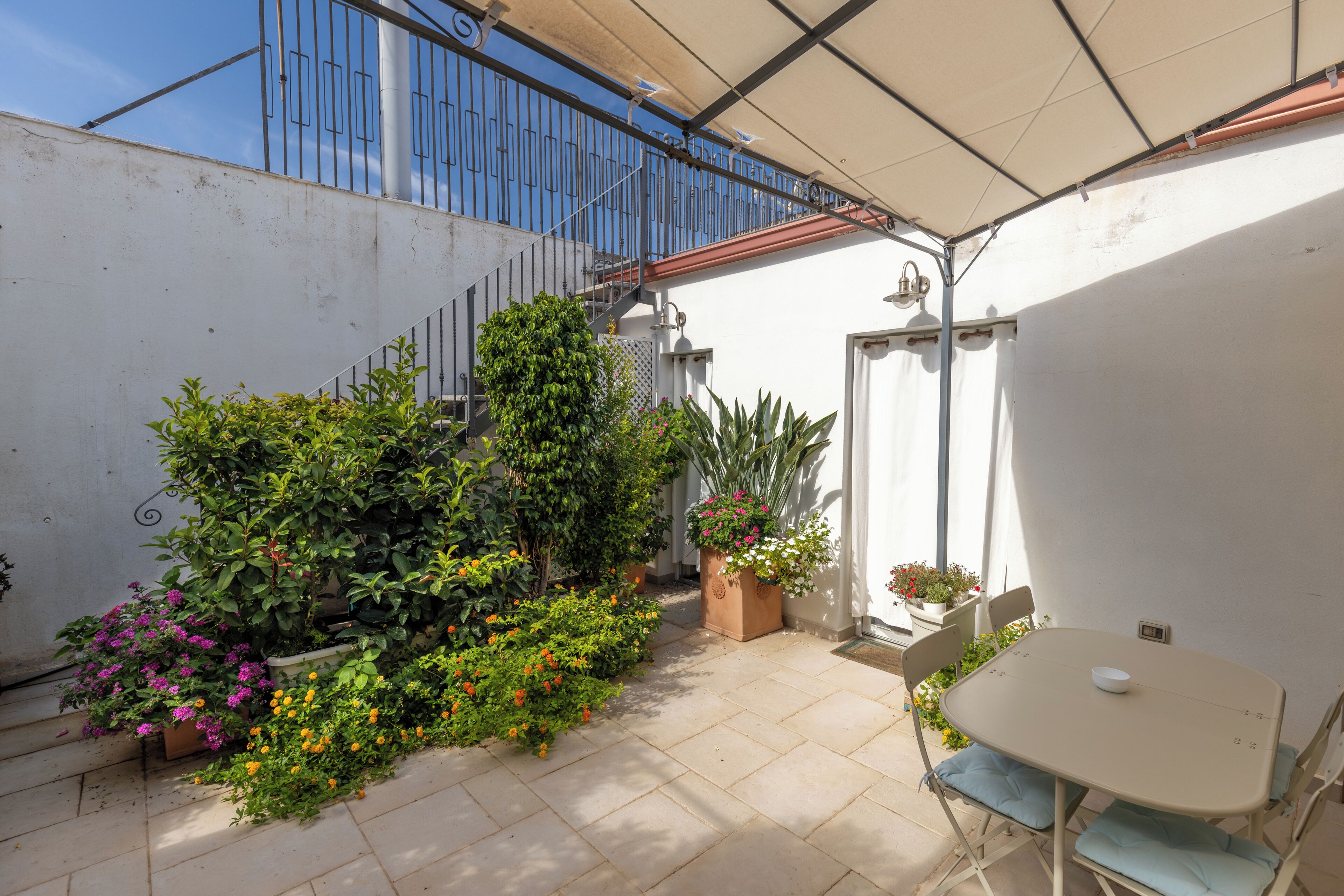 Una terrazza con tavolo e sedie, circondata da piante in vaso e una scalinata.