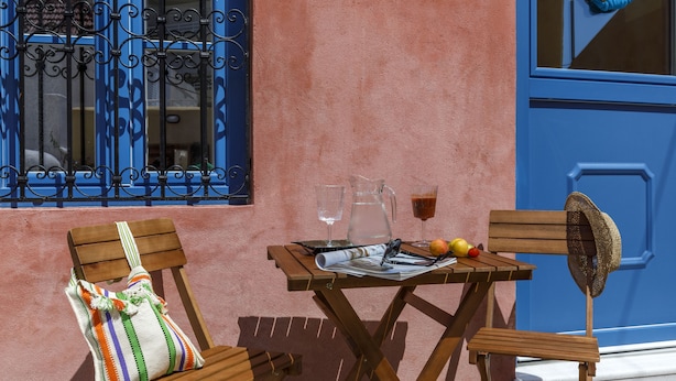 A wooden table with a newspaper, a pitcher, and glasses. Two wooden chairs with cushions are placed beside the table. - Ai Yanni Boutique Rooms - Adults Only (Rhodes)