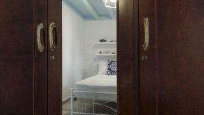 A bedroom with a bed, wooden wardrobe, and a white ceiling light. - Ai Yanni Boutique Rooms - Adults Only (Rhodes)