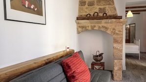 A cozy living room with a stone fireplace, a grey sofa, and a red pillow. - Ai Yanni Boutique Rooms - Adults Only (Rhodes)