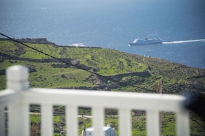 A coastal landscape with a ship in the distance, a white fence in the foreground, and a small building on the hillside. - Villa Zeus (Mykonos)