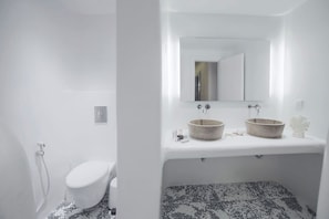 A modern bathroom with a white toilet, a sink with two bowls, and a mirror above the sink. - Villa Zeus (Mykonos)