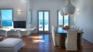 Sala moderna com uma televisão grande, assentos confortáveis e área de refeições com vista para o mar.