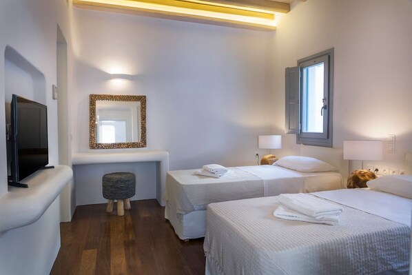 Habitación de hotel con dos camas, televisión, espejo, ventana y un taburete pequeño.