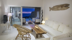 A modern living room with a white sofa, wooden coffee table, wicker chairs, and a television on a white stand. - Villa Athena (Mykonos)