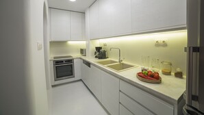 A modern kitchen with white cabinets, a built-in oven, a double sink, and a countertop with a fruit bowl. - Villa Athena (Mykonos)
