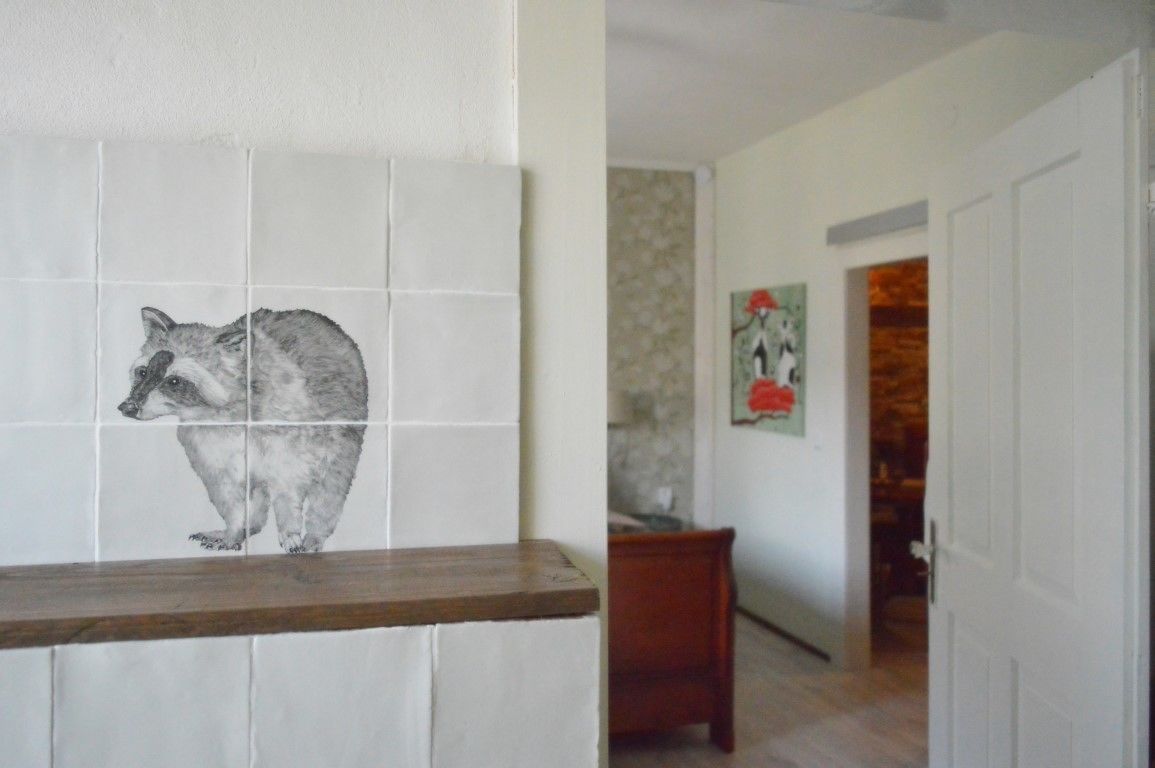 A hallway with a tiled wall featuring a raccoon illustration, a wooden bench, and a door leading to another room.