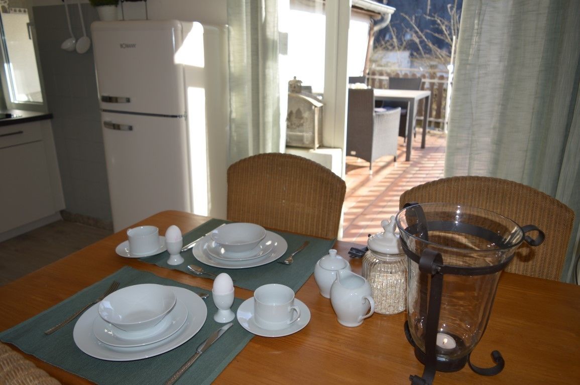 A dining area with a table set for four, including plates, cups, and cutlery. A coffee pot and a candle are also visible.