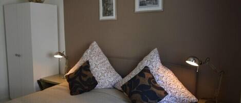 A bedroom with a bed, two bedside lamps, a nightstand, a wardrobe, and two framed pictures on the wall.