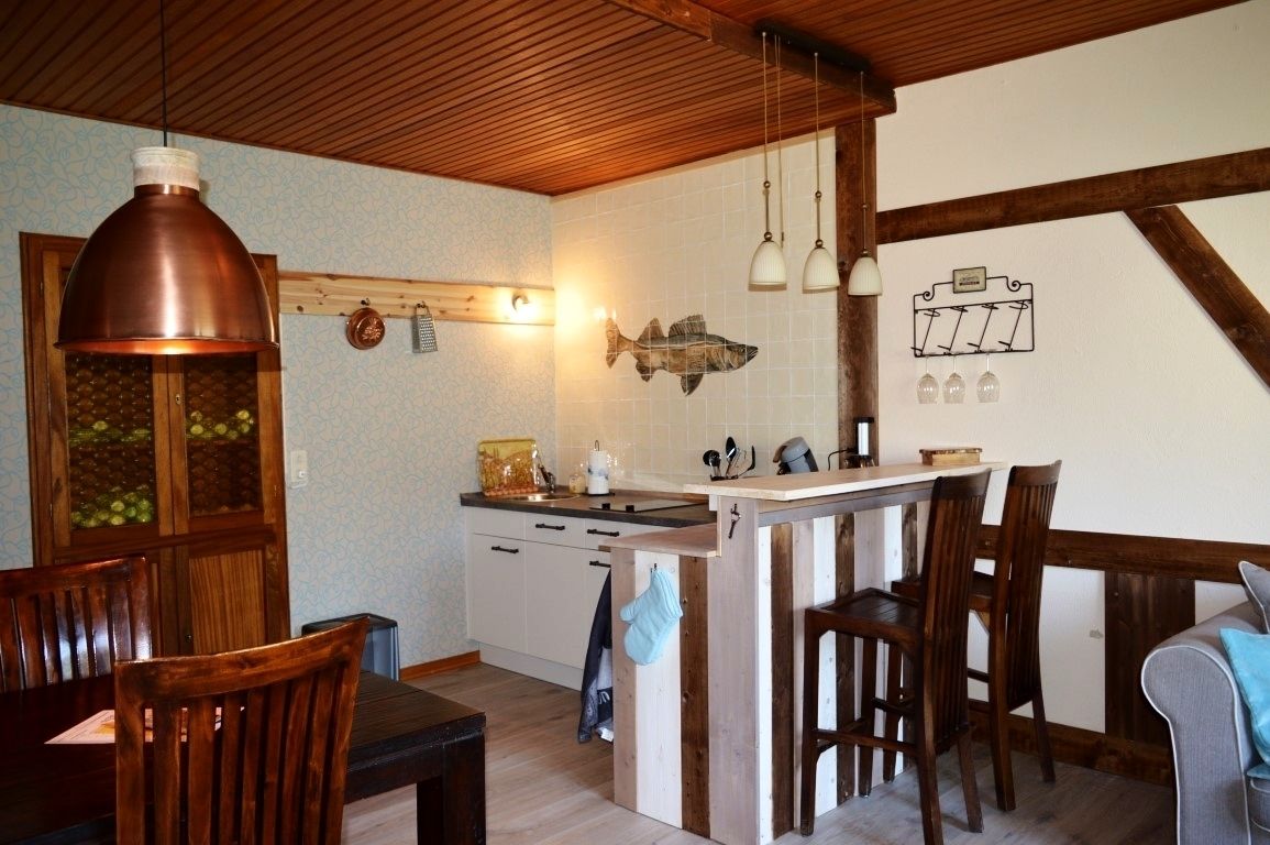 A kitchen with wooden cabinets, a wooden dining table with chairs, a hanging copper light fixture, and a fish-shaped wall decoration.
