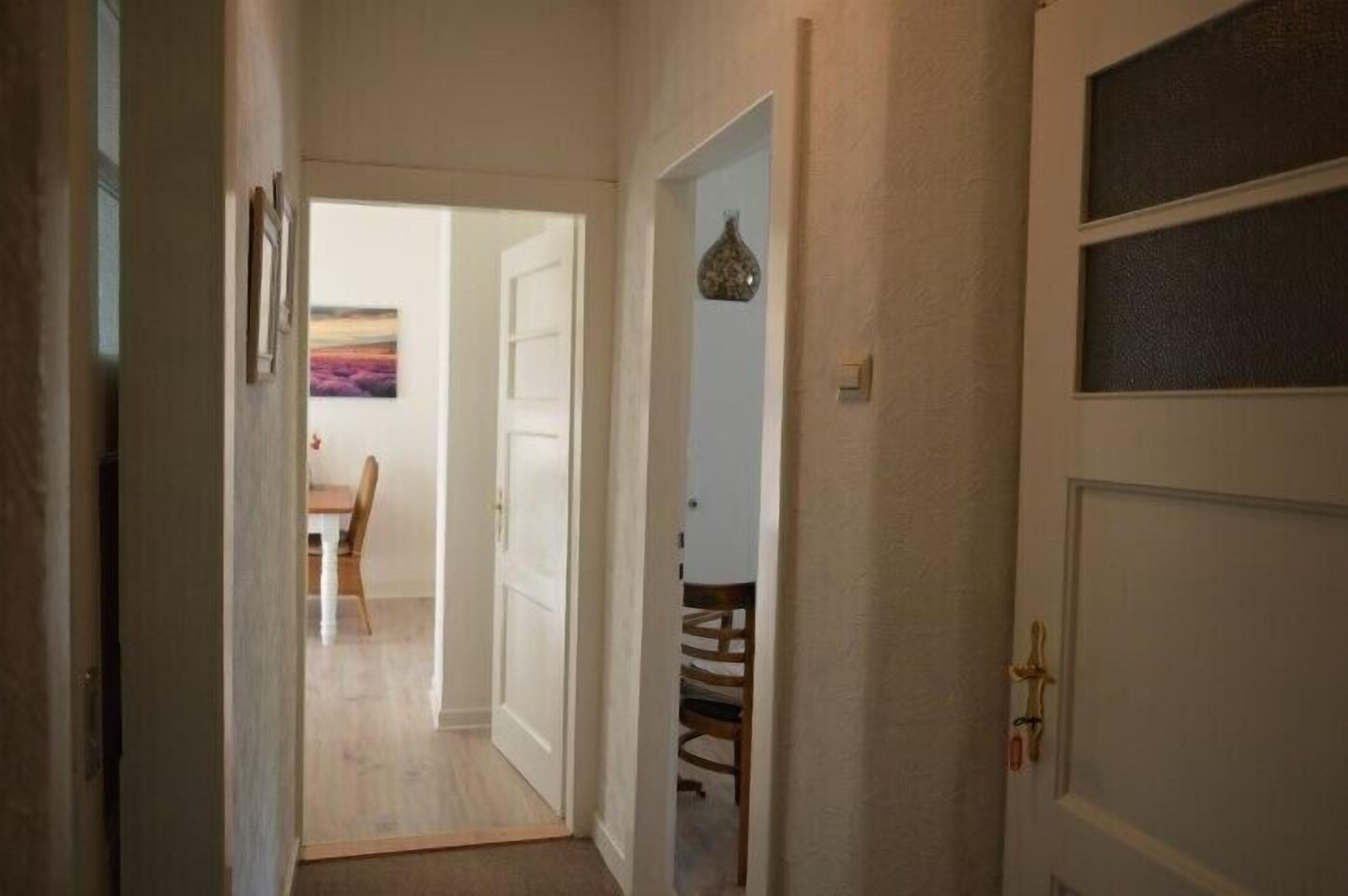 A hallway with a dining area visible through an open door, featuring a table and chairs.
