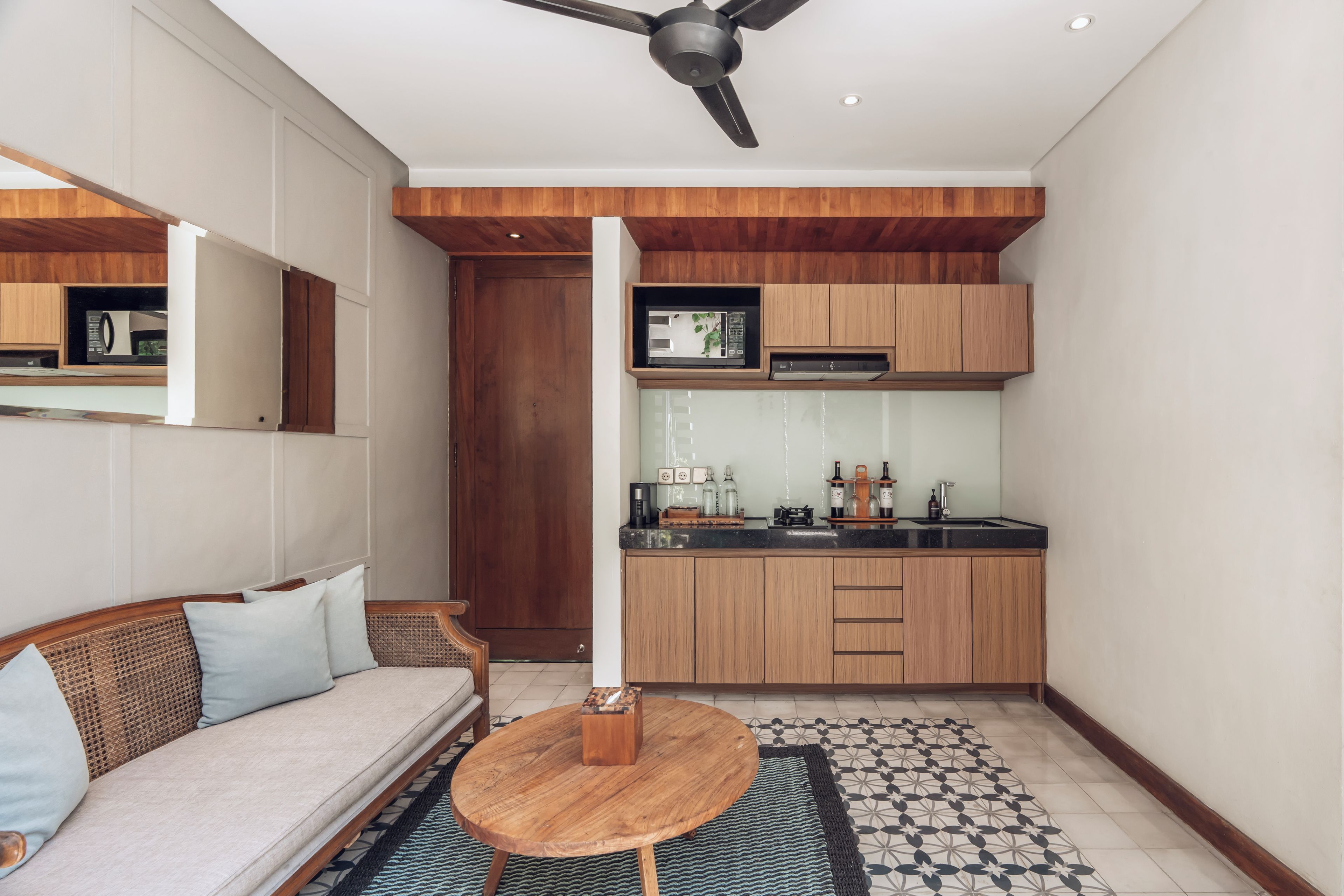 A compact living space with a kitchenette, a dining area with a round wooden table, and a sofa with cushions.