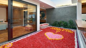 Un interior moderno con un vidrio que da a una habitación, una pared de concreto y un arreglo floral con forma de corazón en el suelo.
