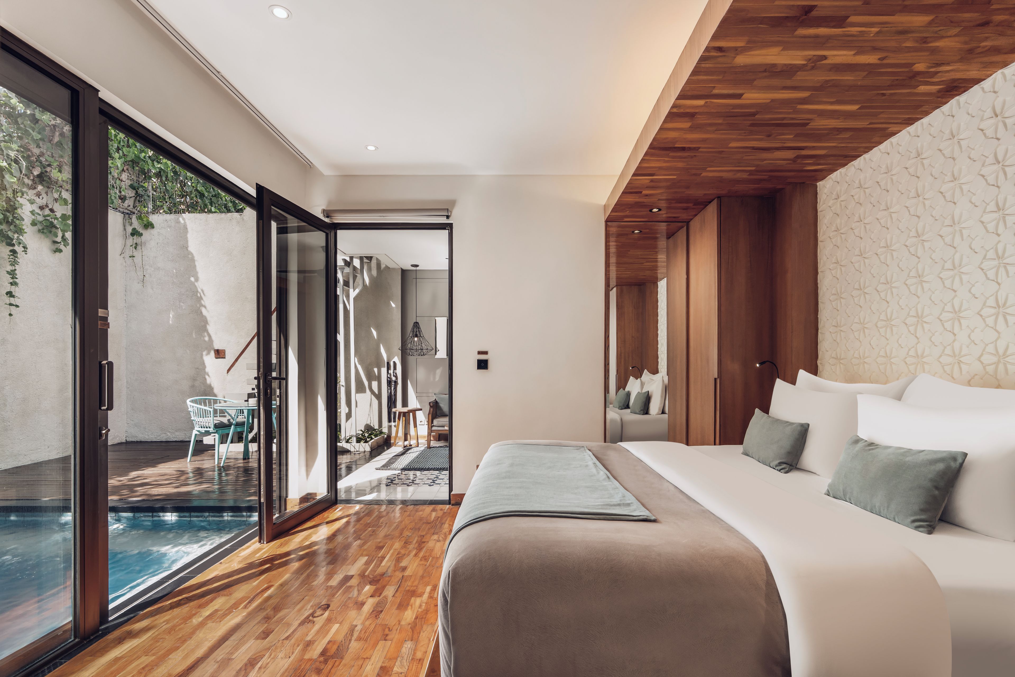 Un dormitorio moderno con una cama grande, suelo de madera y puerta corrediza de vidrio que da a una zona de piscina.