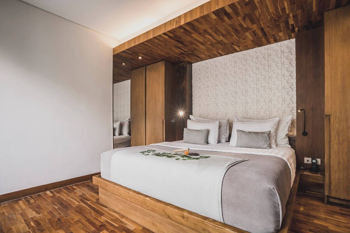 A modern bedroom with a wooden ceiling, a patterned wall, a bed with pillows, and a bedside table with a phone.