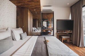 A modern hotel room with a large bed, a TV, and a bathroom visible through an open door. - Ayona Villa Seminyak by Ini Vie Hospitality (Kerobokan)