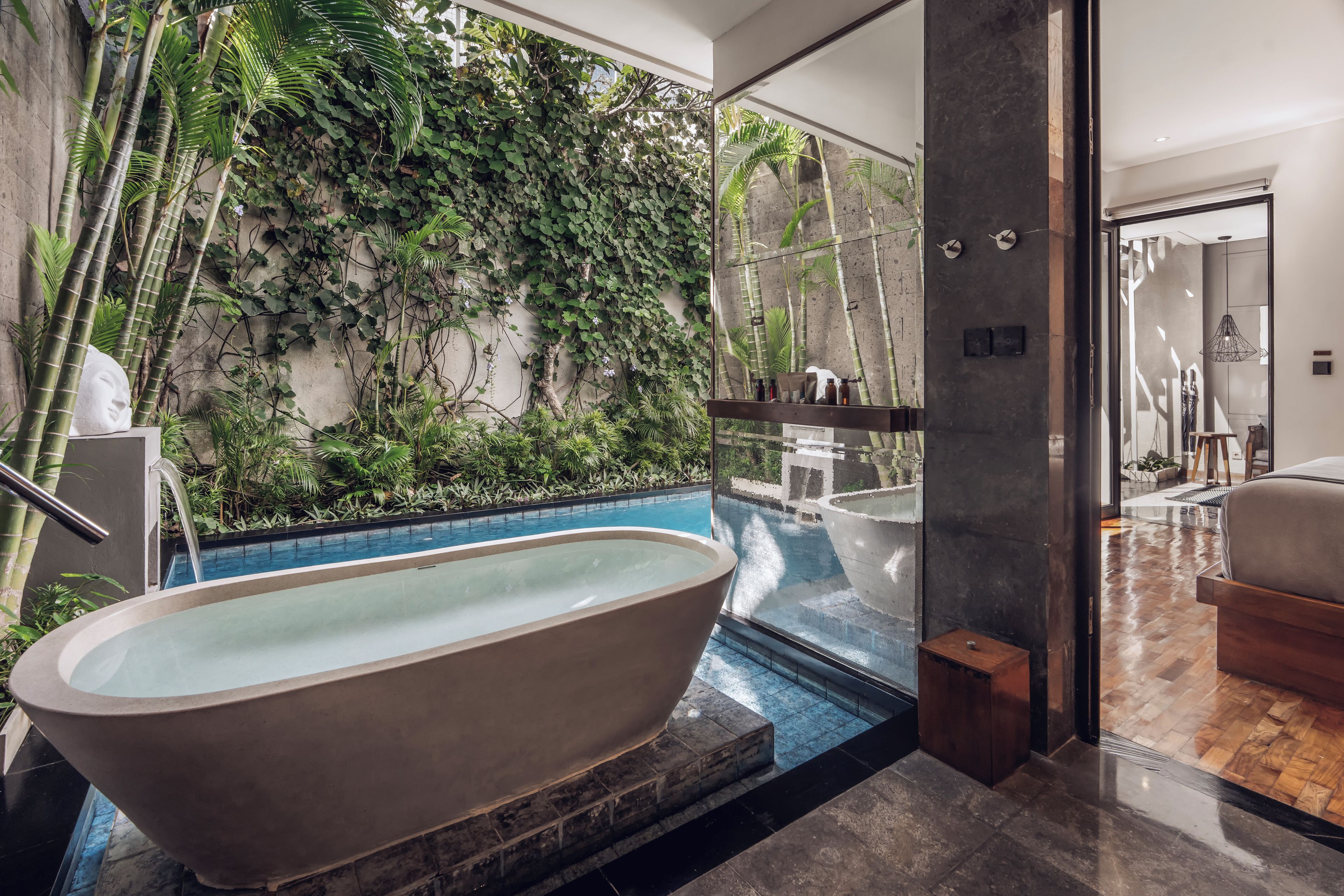 Une salle de bain moderne avec une baignoire sur pieds, une douche à l’italienne et un mur recouvert de plantes.