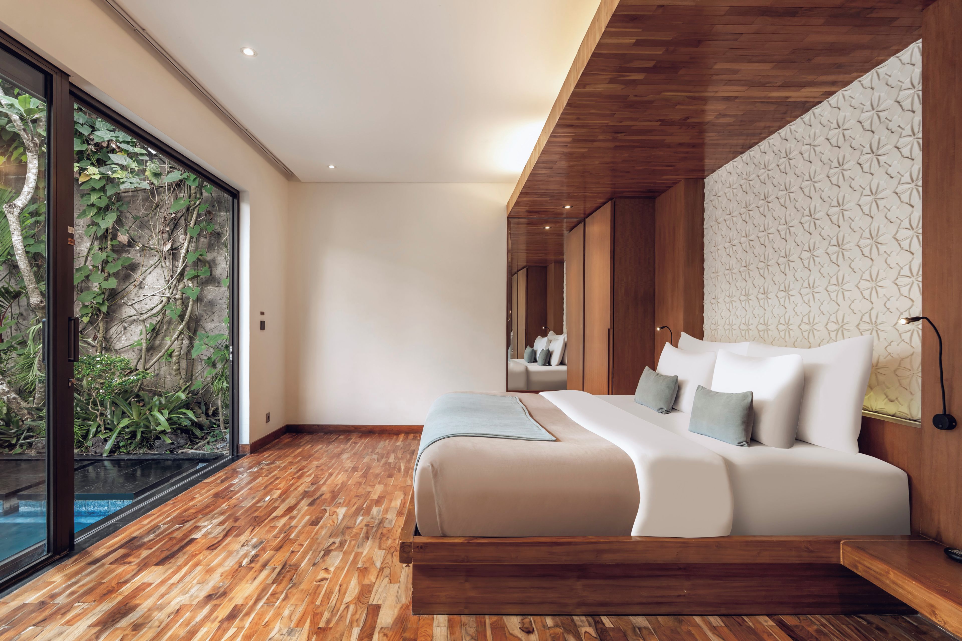 Une chambre moderne avec un grand lit, un plancher en bois et une vue sur la verdure grâce à une porte vitrée.