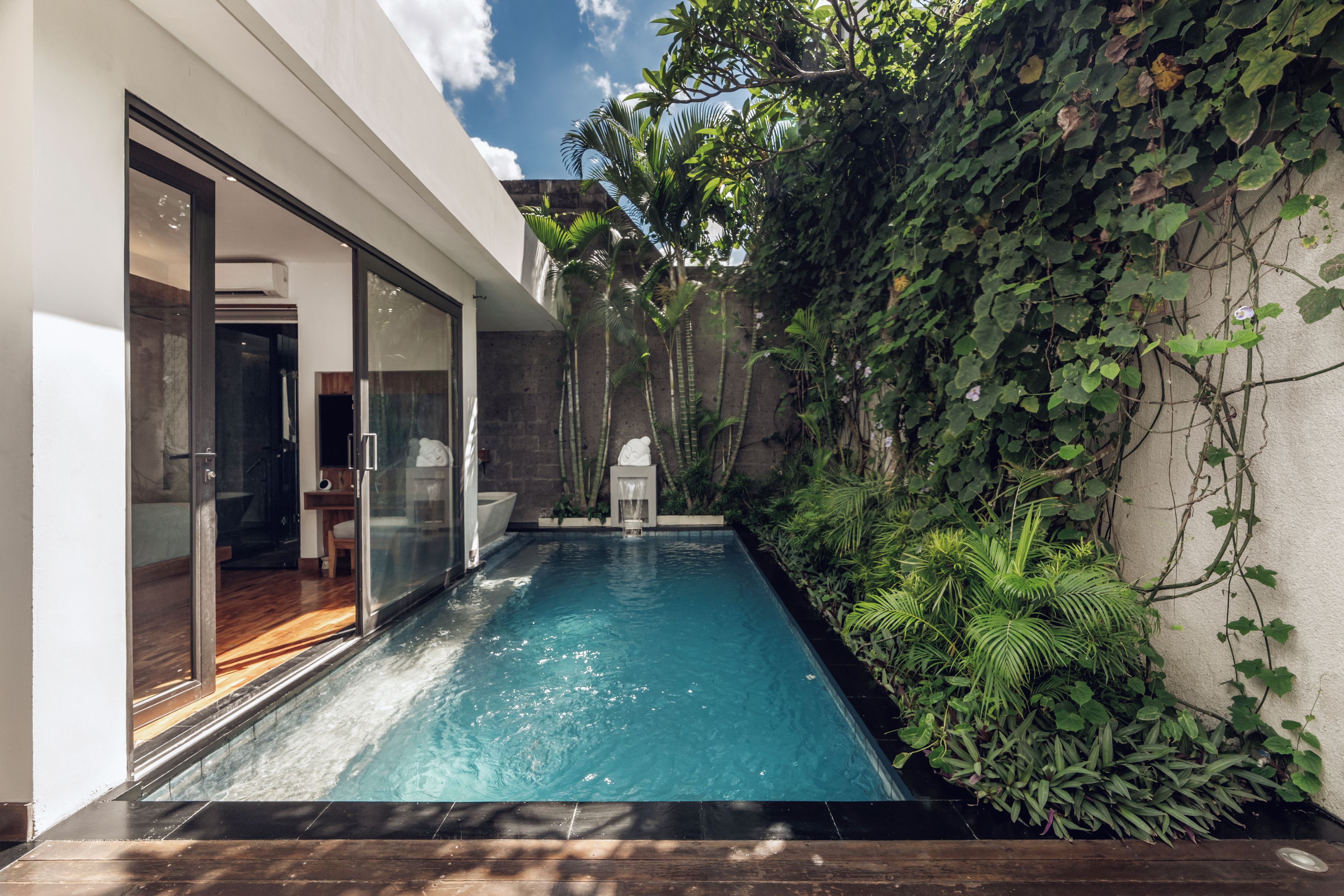 Una piscina moderna con puertas de vidrio que dan a una habitación, rodeada de exuberante vegetación.