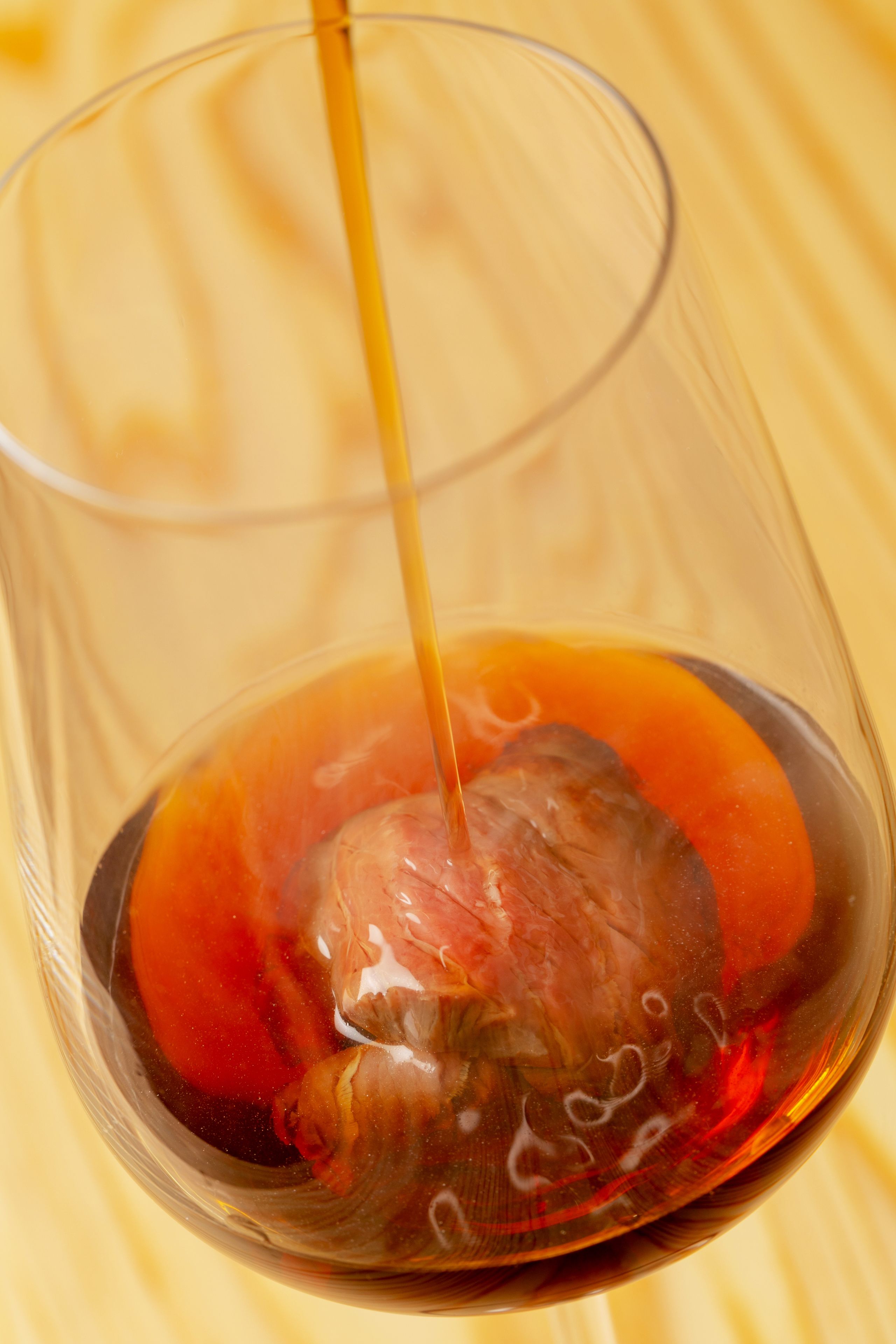 A glass with a dark liquid and a spherical object, possibly a fruit, on a wooden surface.