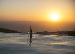 A bottle of champagne and two glasses on a reflective surface with a sunset view in the background. - Villa Aphrodite (Mykonos)