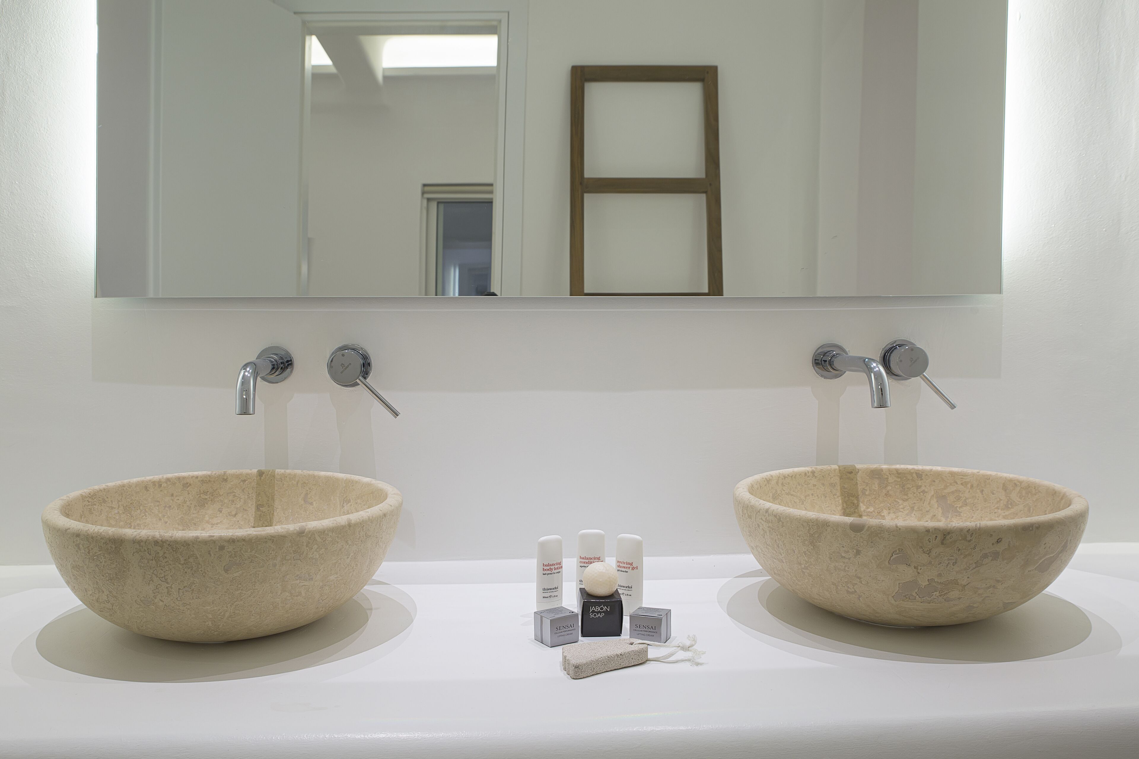 A bathroom with two beige ceramic sinks, a mirror above, and a small shelf with toiletries.