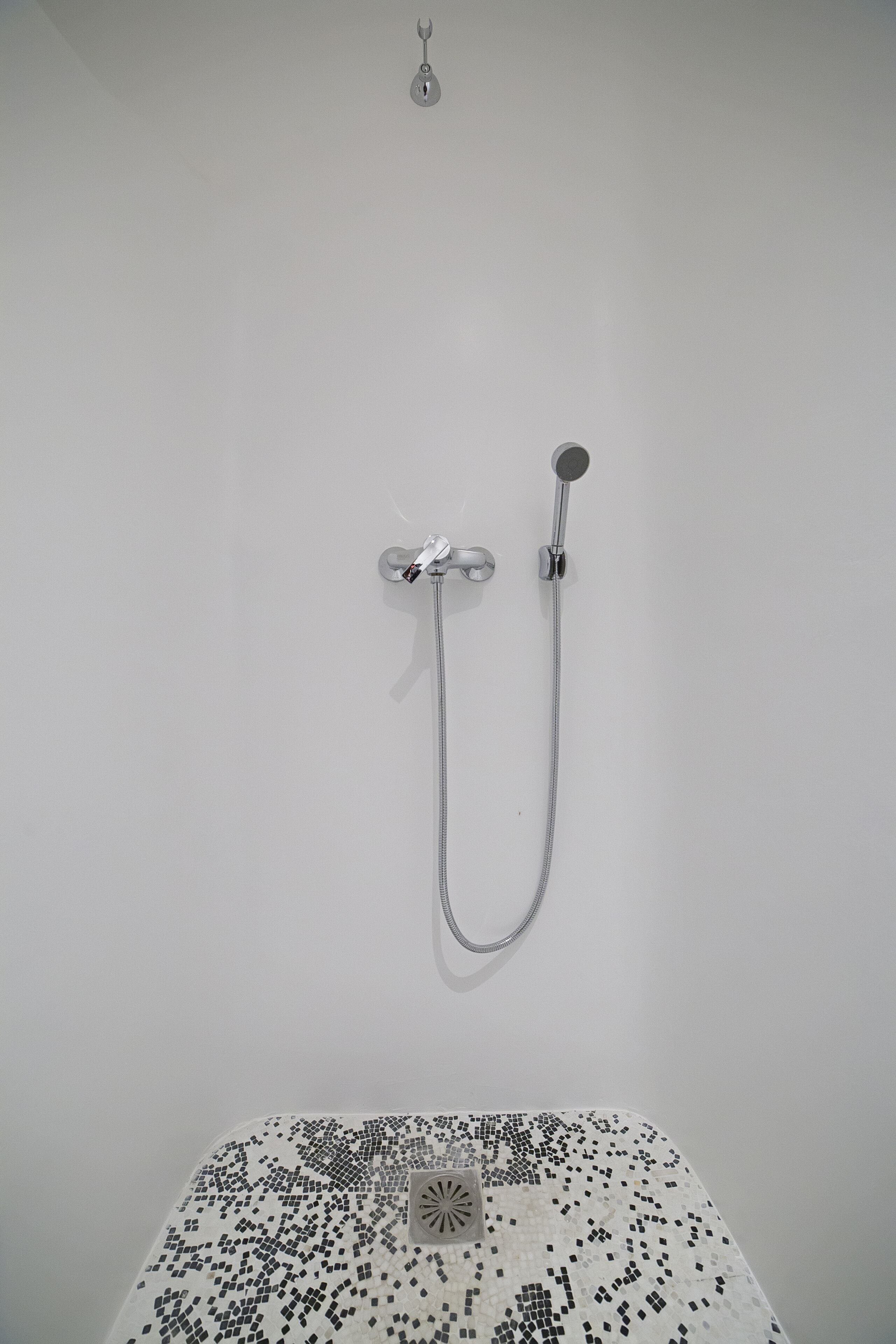A shower with a handheld showerhead and a wall-mounted faucet.