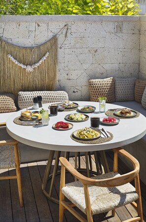 A round outdoor dining table with various dishes, surrounded by woven chairs and cushions. - Kaipo Alacati (Cesme)