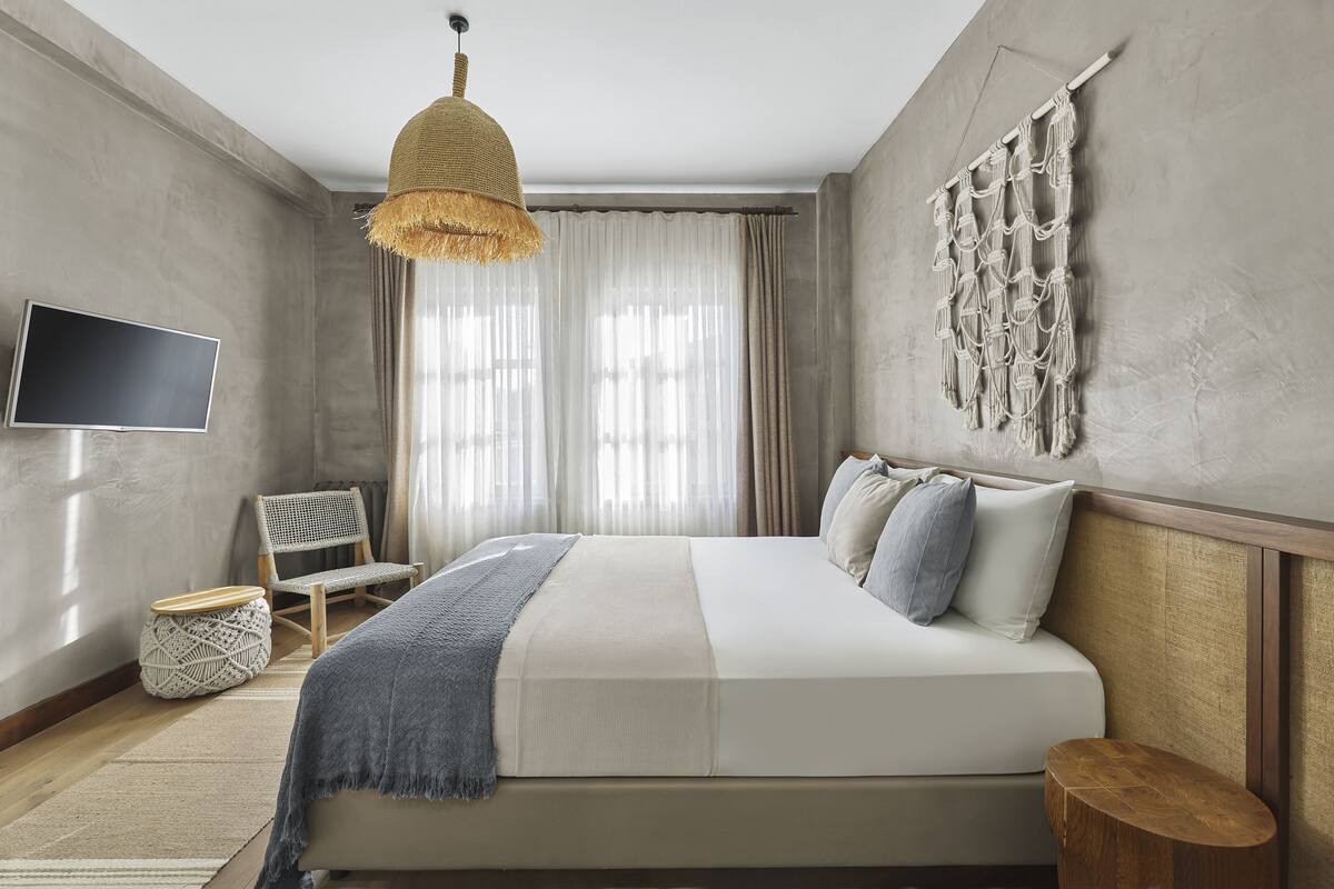 Un dormitorio moderno con una cama grande, un televisor, una lámpara de fibra natural y un tapiz de macramé en la pared.