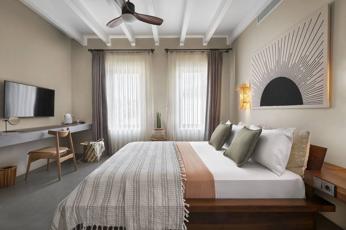 Una habitación de hotel moderna con cama, escritorio, silla, televisor y obras de arte.