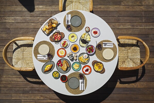 A round table with various dishes and bread, surrounded by wicker chairs on a wooden deck. - Kaipo Alacati (Cesme)