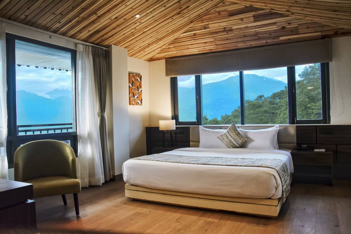 A bedroom with a large bed, a chair, a nightstand, and a window with a mountain view.