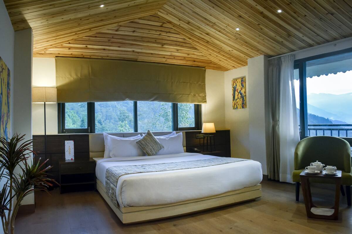 A spacious bedroom with a large bed, wooden ceiling, and a view of mountains through the window.