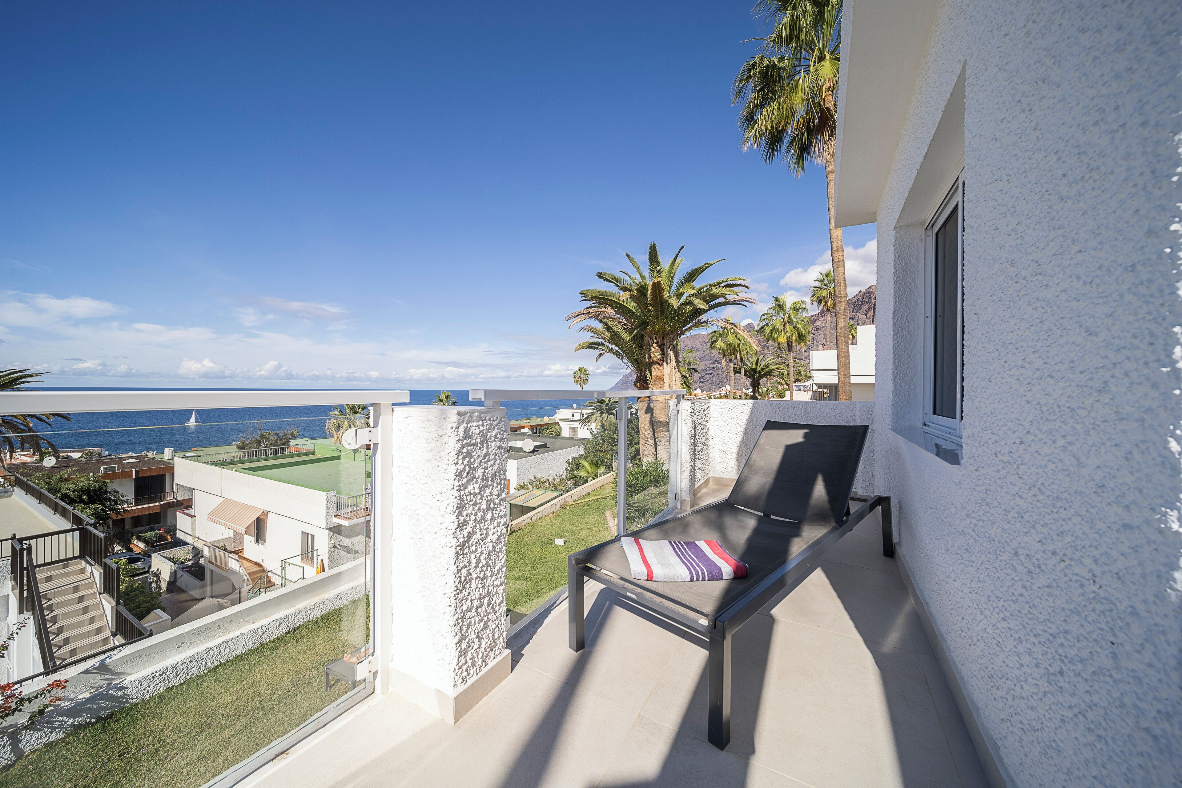A balcony with a view of the sea, a lounge chair, and a small garden area.
