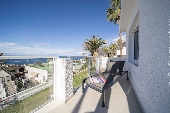Un balcón con vistas al mar, una silla de descanso y una pequeña zona ajardinada.