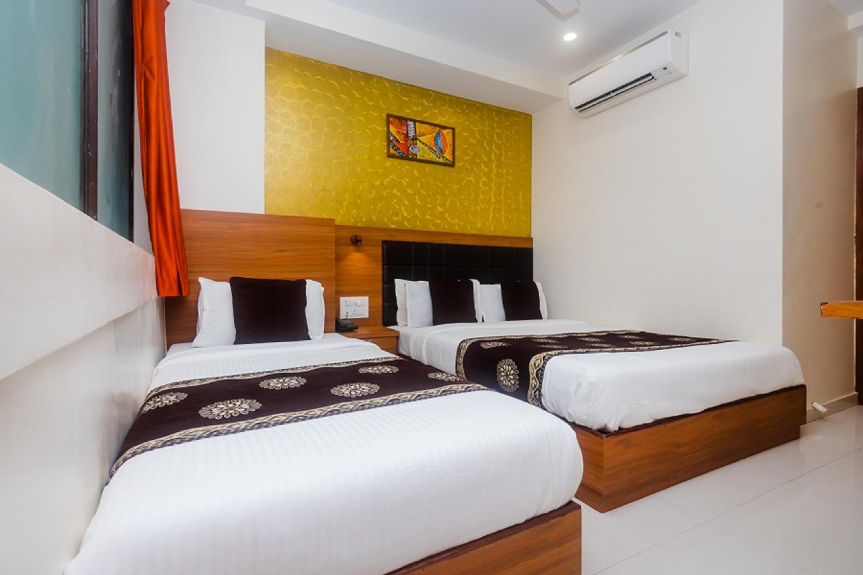 A hotel room with two beds, a wooden headboard, a yellow textured wall, and an air conditioning unit.