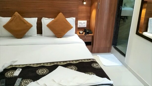 A hotel room with a bed, a bedside table with a phone, and a window. - Hotel Aiston Inn (Mumbai)
