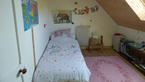 Ett mysigt sovrum på vinden med ett sluttande tak, en säng med ett sängöverkast med enhörningstema, en liten trästol, ett element och en bokhylla.