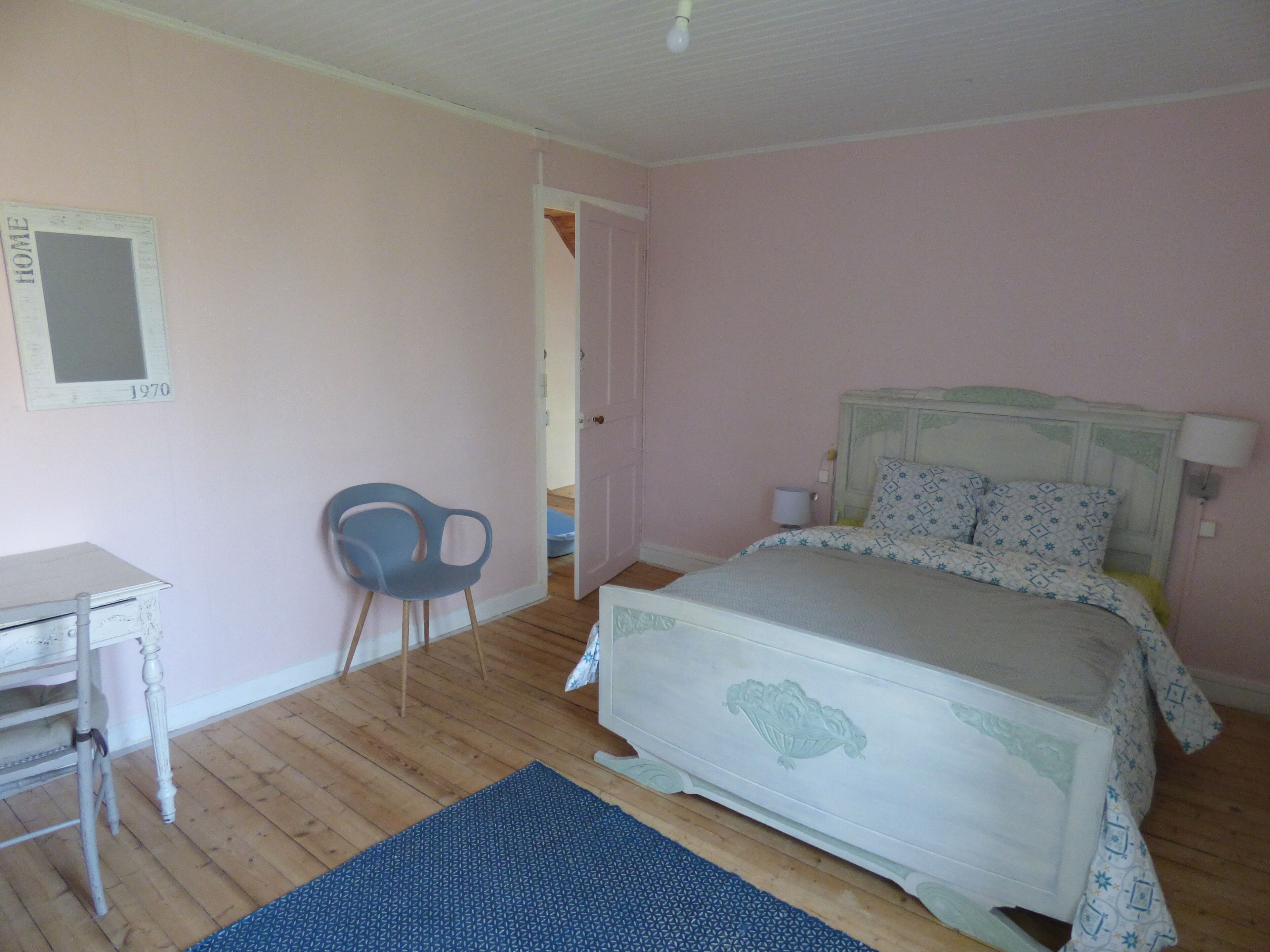A bedroom with a bed, a desk, a chair, and a door leading to another room.