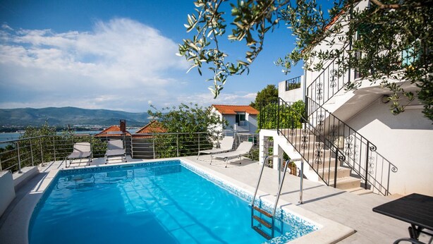 A swimming pool with a view of mountains, a white building with balconies, and a clear sky. - Villa with sea view and swimming pool (Trogir)