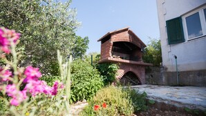 A brick-built outdoor oven structure in a garden setting with a white building in the background. - Villa with sea view and swimming pool (Trogir)