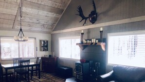 Una sala de estar acogedora con chimenea, un comedor con mesa y sillas, y un amplio ventanal con persianas.