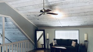 Amplia sala de estar con techo de madera, ventilador de techo, sofá verde oscuro con almohadones decorativos, mesa de centro de madera y un espejo grande.