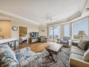 A spacious living room with a large window, a ceiling fan, and a dining area with a TV.