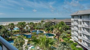 Een resort met meerdere zwembaden, omgeven door palmbomen en uitzicht op strand en zee.